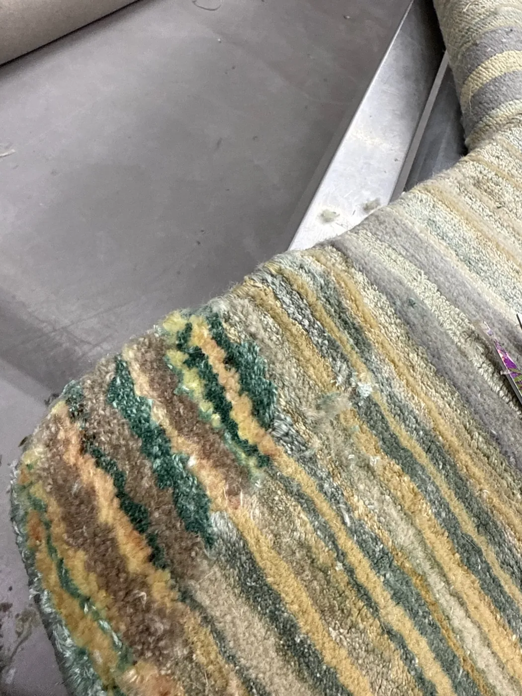 Area of worn pile loss on a green rug, noted at inspection